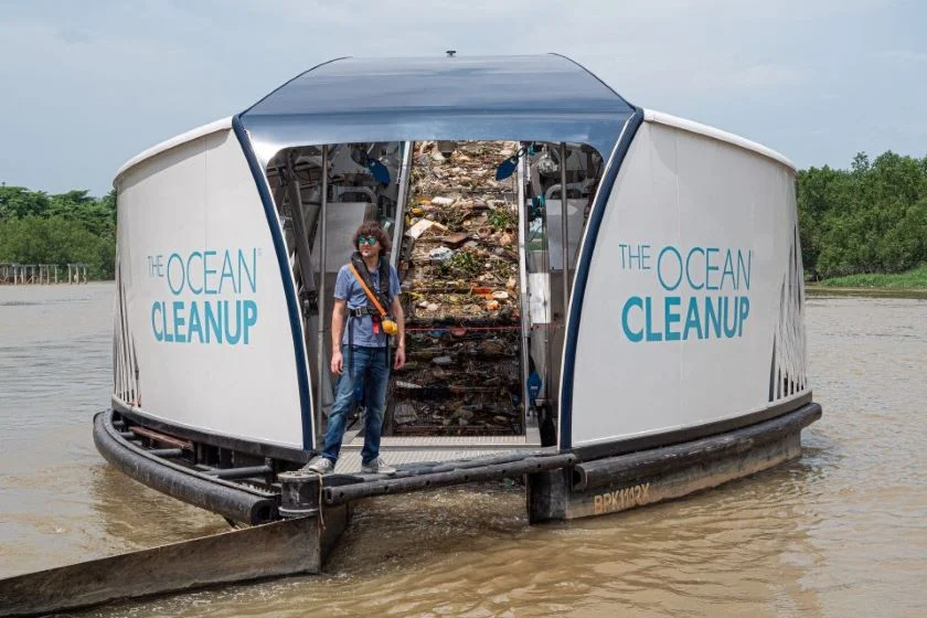 A man standing on a futuristic-looking vessel full of trash floating on brown water.
