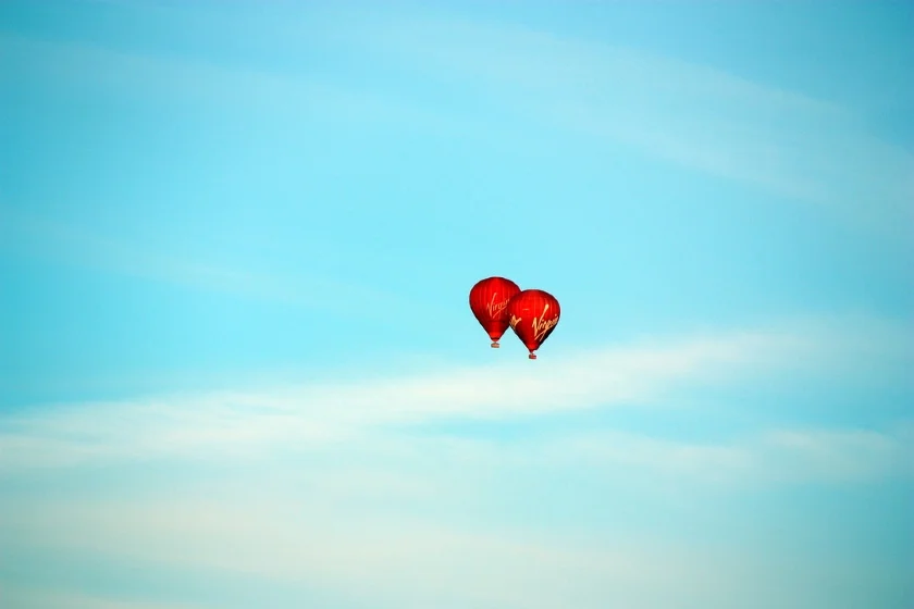 Two hot air balloons branded with the Virgin Airlines logo against a blue sky.