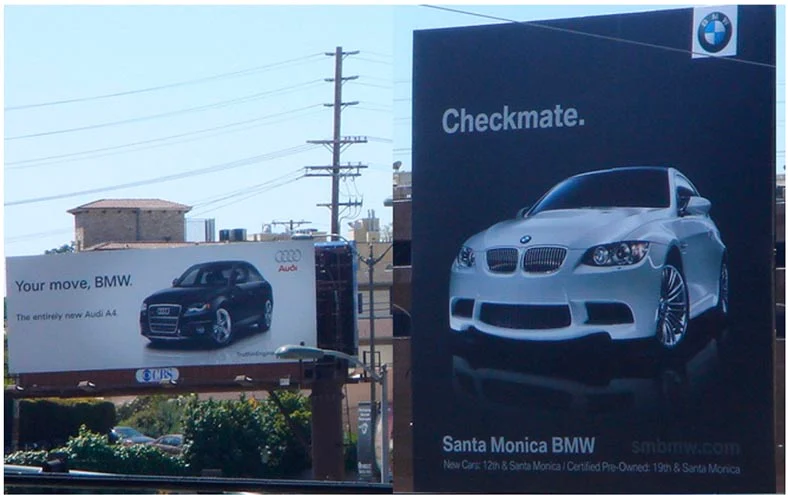 Billboards from Audi and BMW competing against each other on opposite sides of a road.