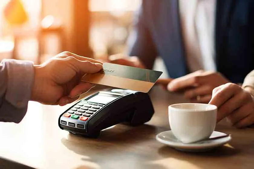 Person holding out a card to a portable payment terminal with a cup of coffee in the foreground.