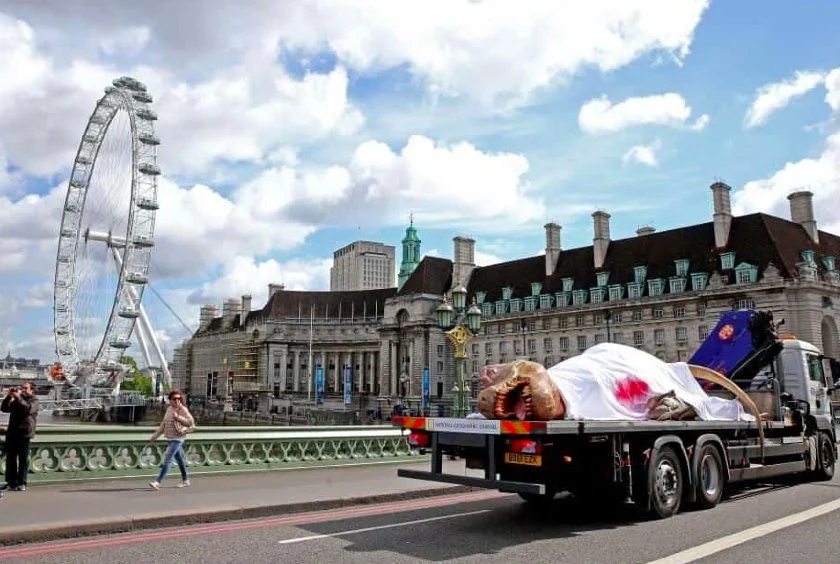 An injured T-Rex being driven on the back of a truck on a London street.