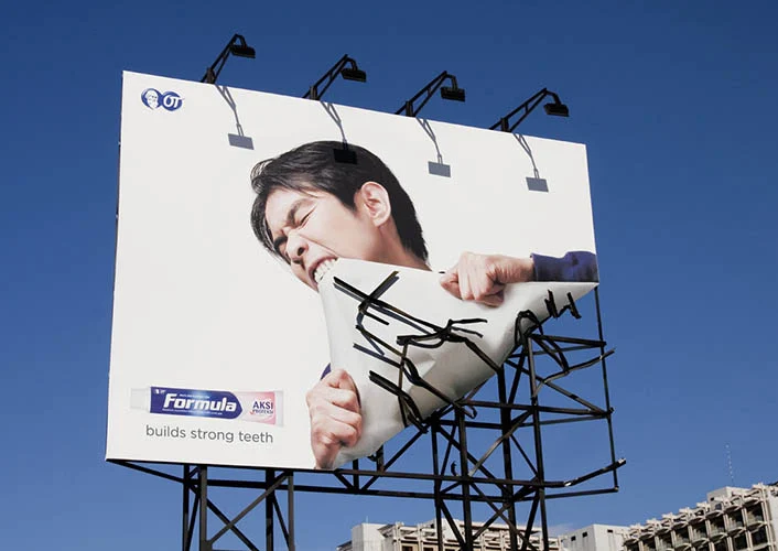 A billboard from a toothpaste brand showing a person tearing off the billboard from its frame using their teeth.