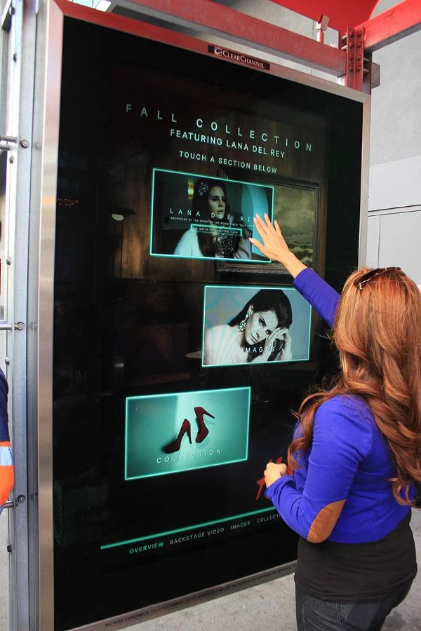A passerby interacting with an interactive billboard on a sidewalk.
